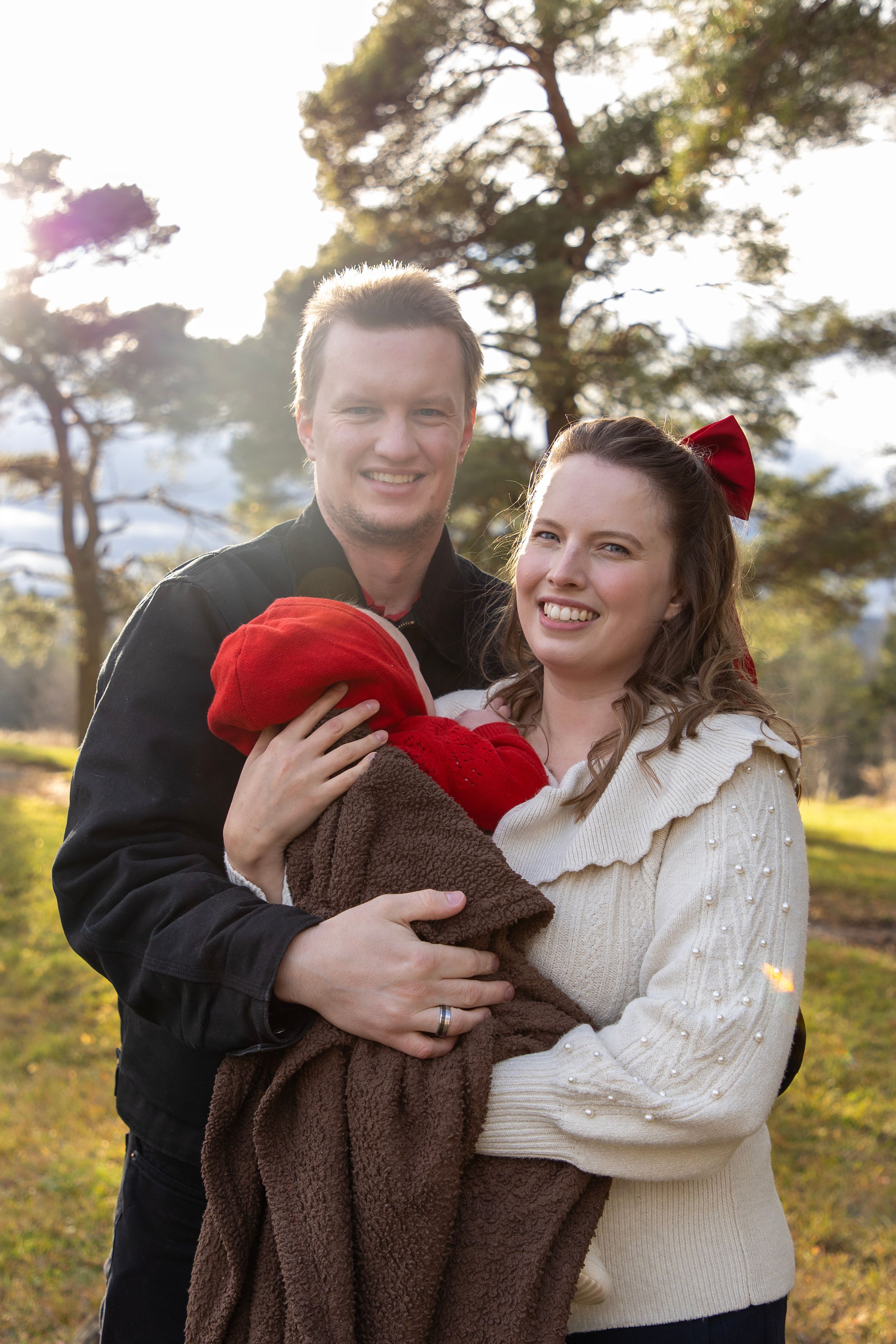 A family photo with 2 new parents. The baby's facing away from the camera wrapped in a brown blanket