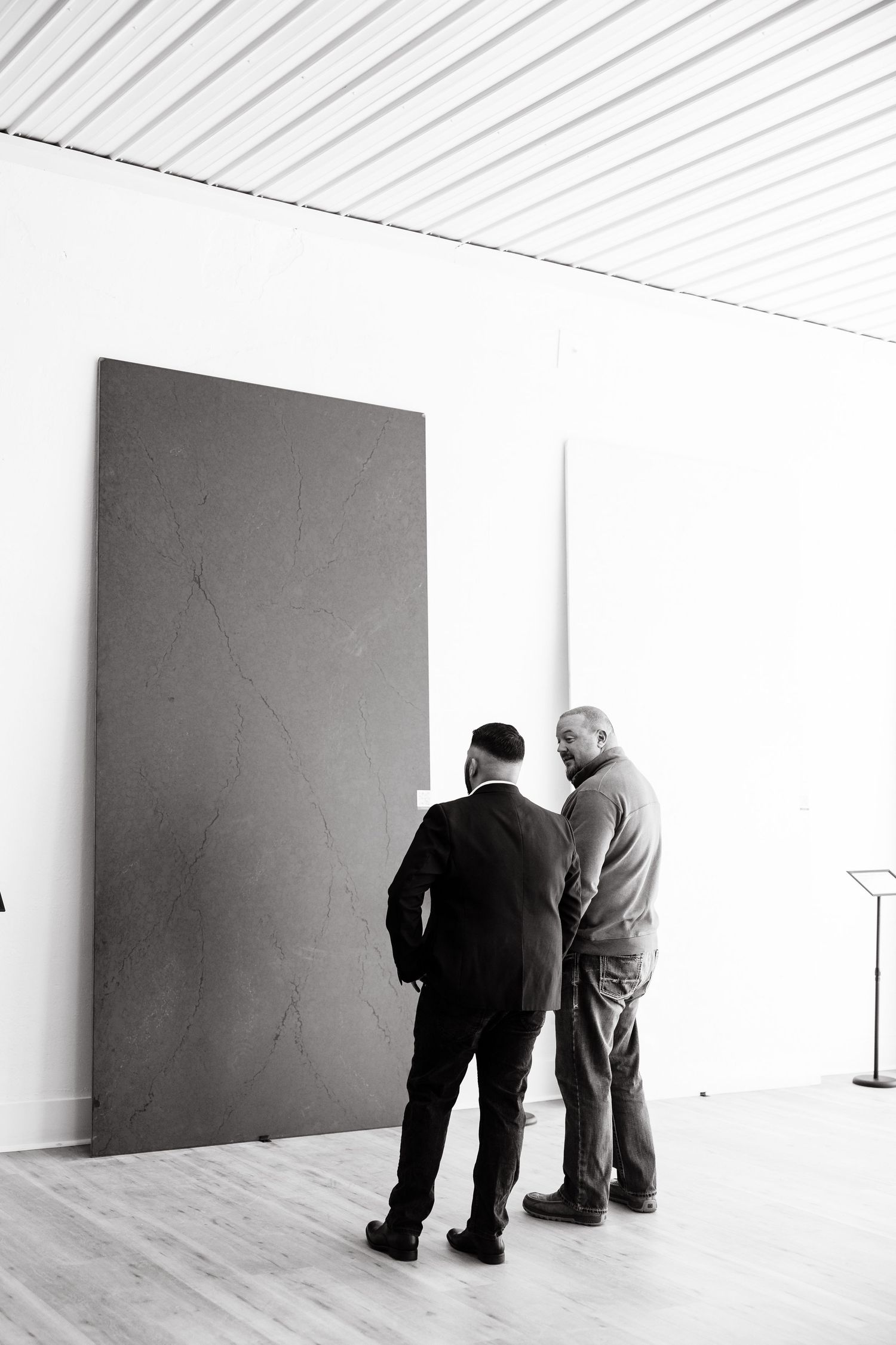 Two figures lean forward to examine a blank white wall in a minimalist gallery space.