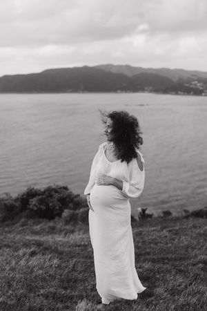 A person in white clothing sits on a grassy hillside overlooking the ocean in a black and white photo series.