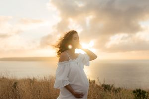 A figure stands in a golden wheat field at sunset with sunlight creating a warm ethereal glow through flowing fabric.