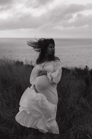 A figure in a flowing white dress dances gracefully through a windswept field against a moody sky.