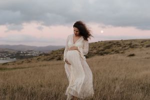 Woman in flowing white dress twirls through a golden field at sunset near the ocean.