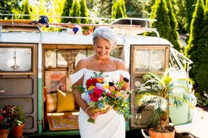 A bright wedding scene with a vintage VW bus decorated with potted plants and colorful floral bouquet.