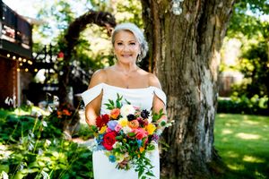 A bride in a white dress holds a vibrant bouquet of flowers while posing in a sunny garden setting.