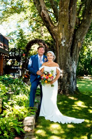 A wedding couple poses under a large tree in a garden setting on a sunny summer day.