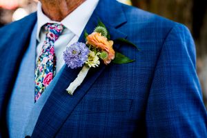 Groomsmen in navy blue suits with colorful floral boutonnieres stand together at a formal wedding.
