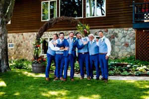 Wedding party members in blue attire gathered on grass lawn outside rustic lodge building.