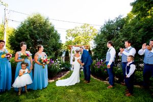 An outdoor wedding ceremony in a garden with attendants in blue dresses and groomsmen in dark suits.