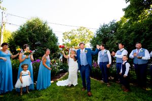 Wedding guests and bridal party gathered outdoors on a sunny day wearing coordinated blue attire.