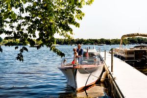 Wedding ceremony setup with white chairs along a scenic lakefront dock on a sunny summer day.