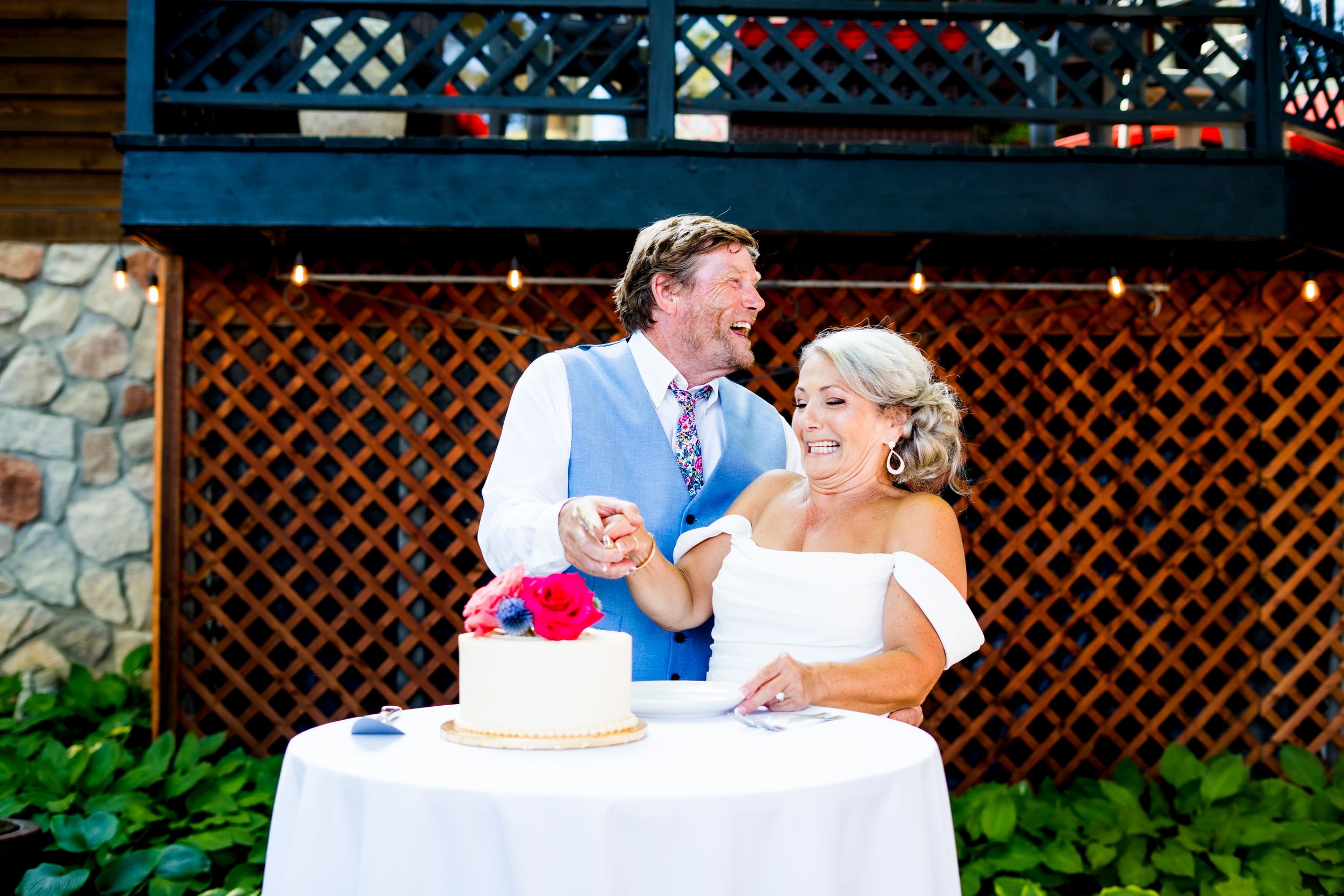 A couple cuts their wedding cake together at an outdoor reception with lattice decor.