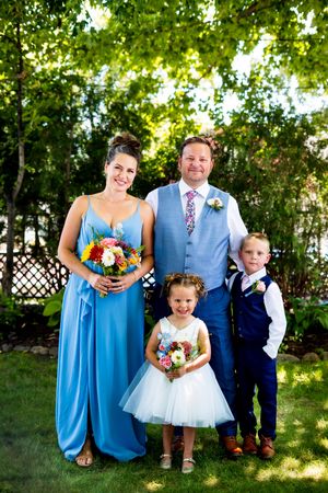 Wedding party members in light blue dresses and suits pose together in a sunny garden setting.