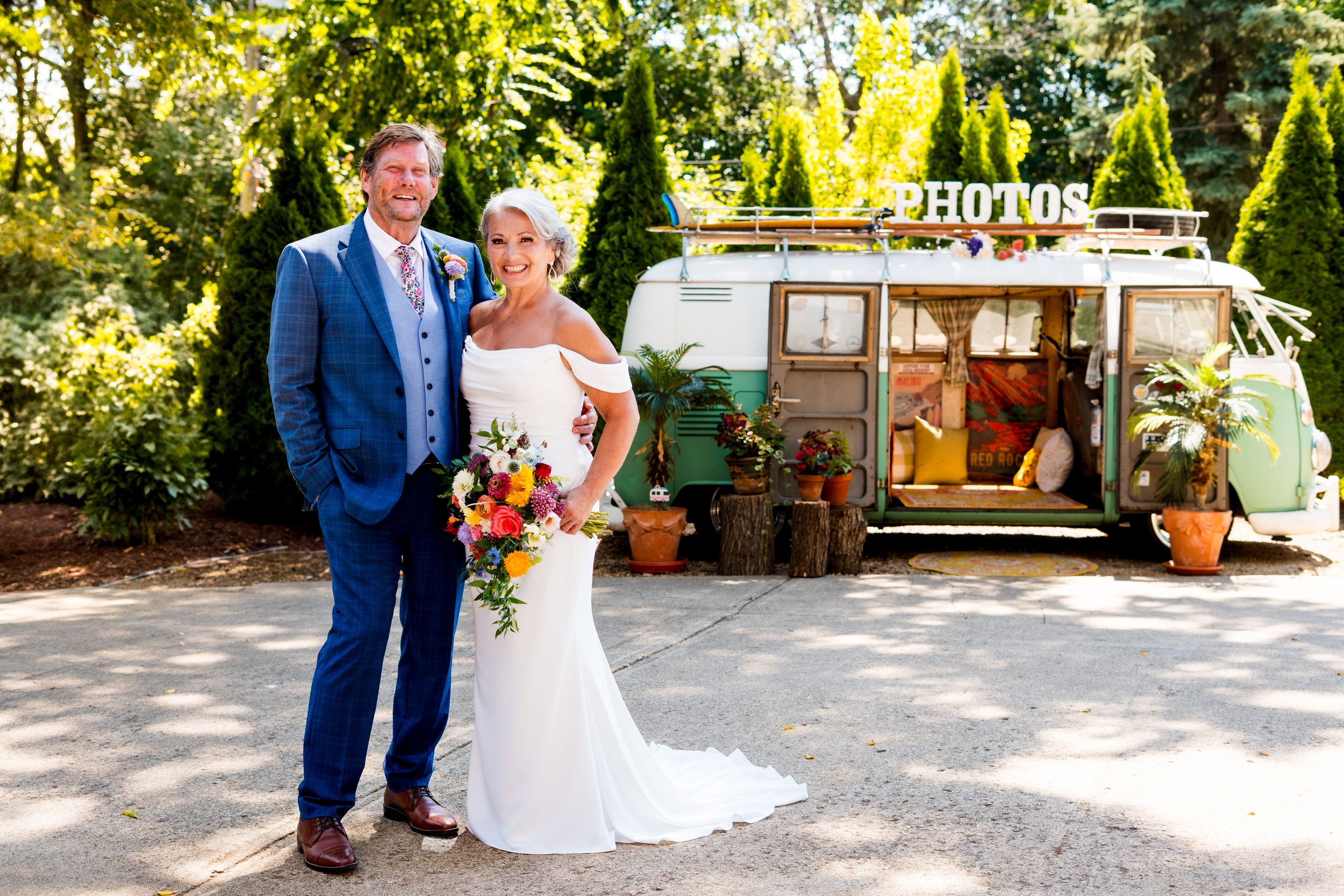 A couple in wedding attire stands together outdoors at a rustic venue on their special day.