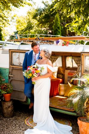 Couple in wedding attire sharing a romantic moment on an outdoor patio decorated with colorful flowers and greenery.