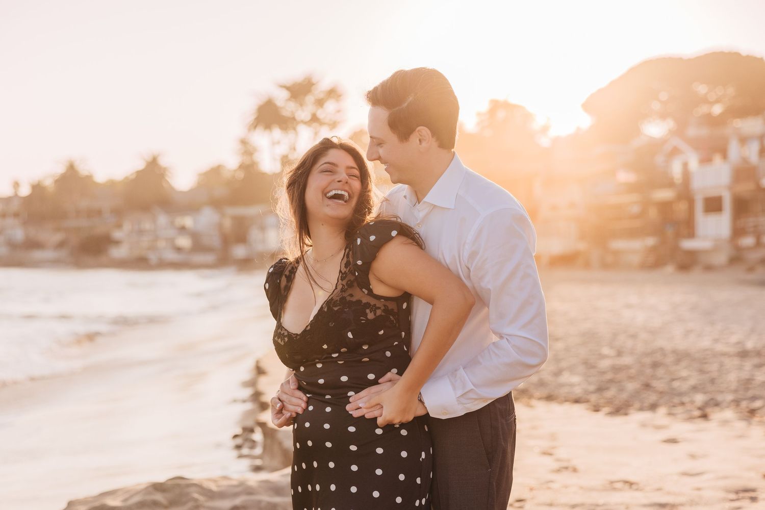 A couple shares a joyful moment together on the beach during golden hour sunset at Miramar Beach in Santa Barbara, CA
