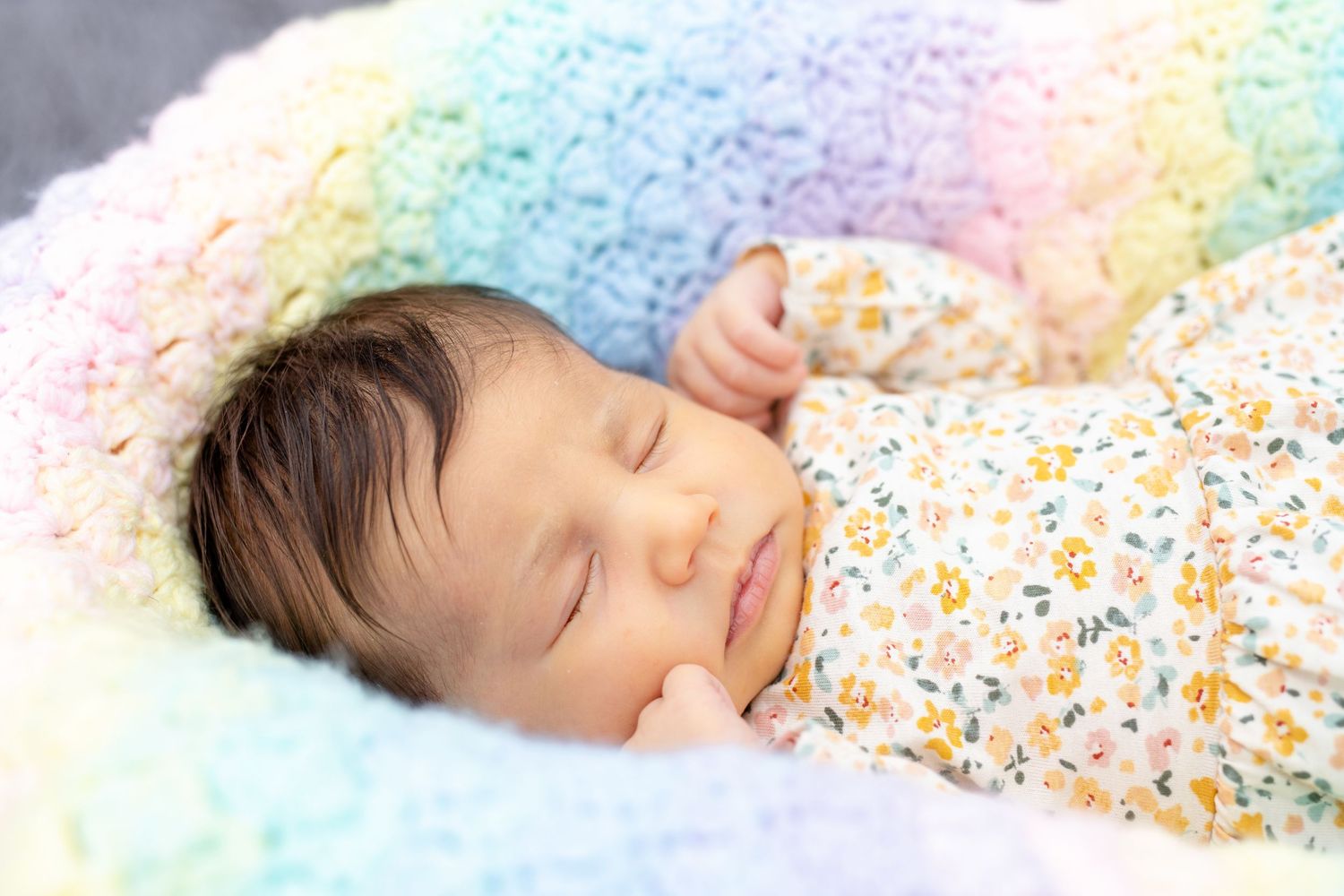Sleeping newborn wrapped in floral print blanket on rainbow colored textured fabric.
