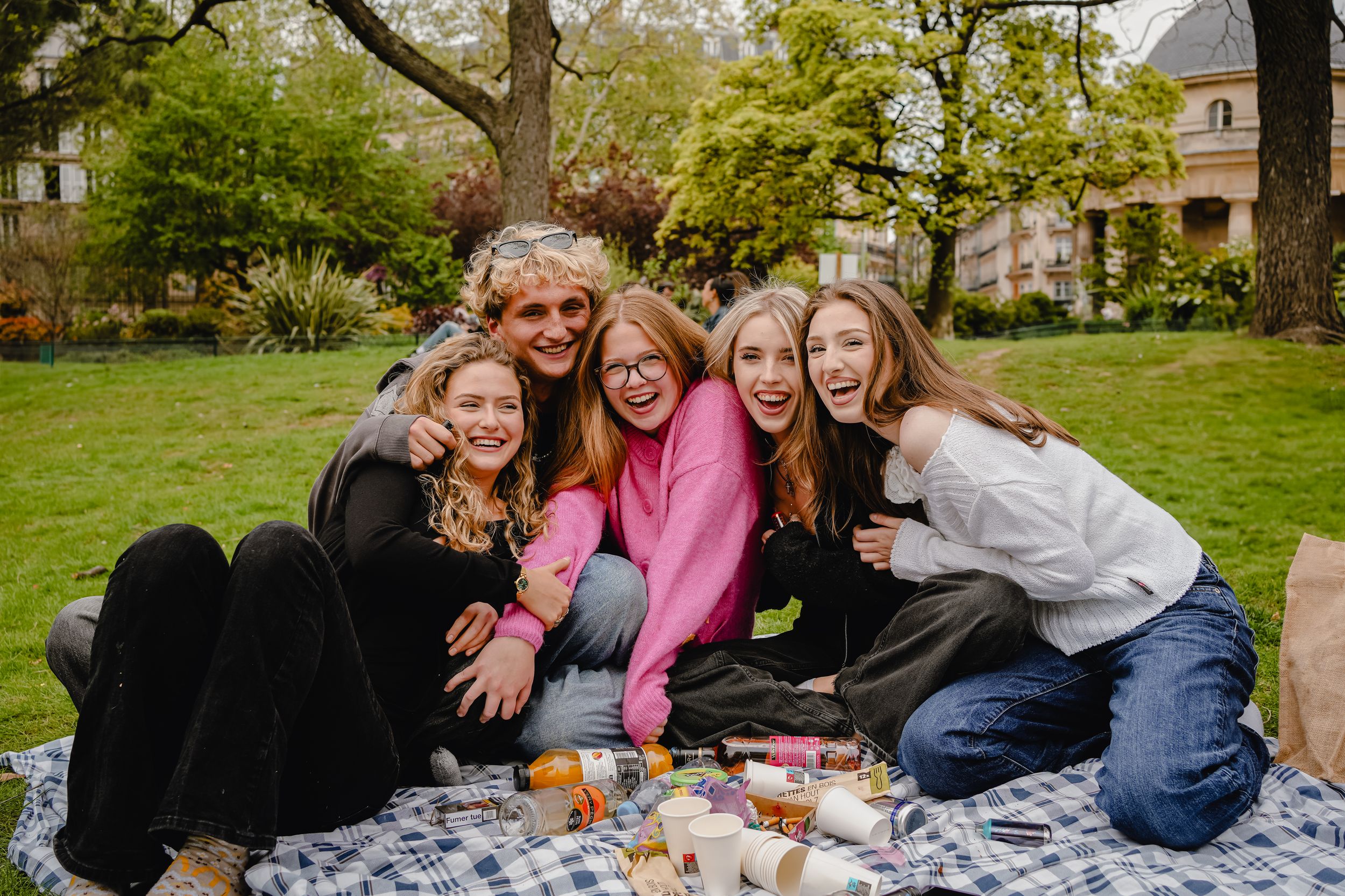 Friends enjoying a casual outdoor picnic gathering on a blanket in a park setting.
