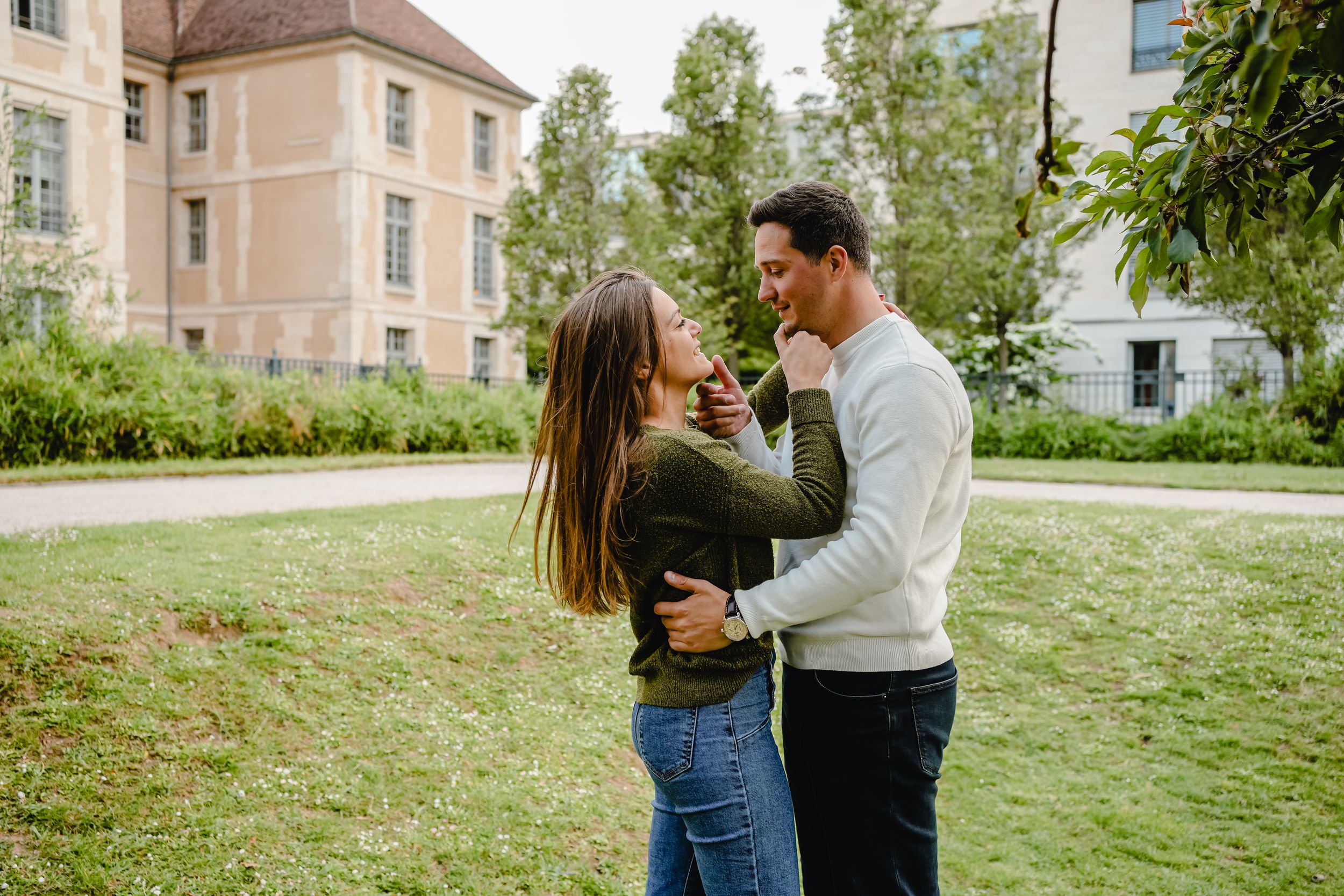 A romantic moment captured in a garden setting with historic buildings in the background.