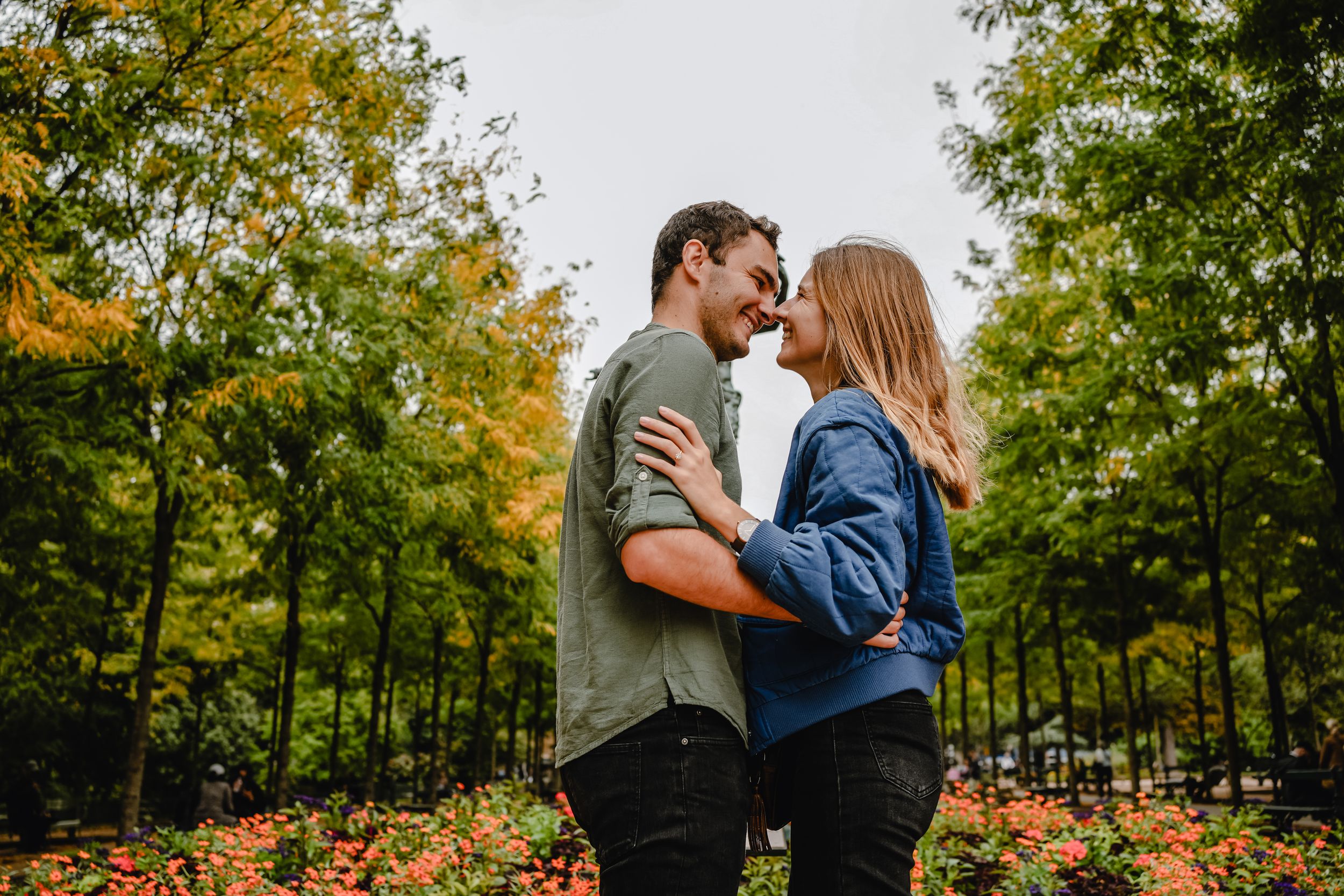 A couple shares intimate moments in a lush autumn park setting with golden leaves in the background.