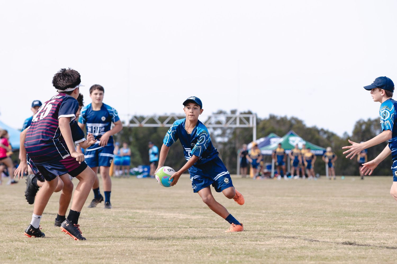Youth athletes playing rugby on dirt field during competitive match.