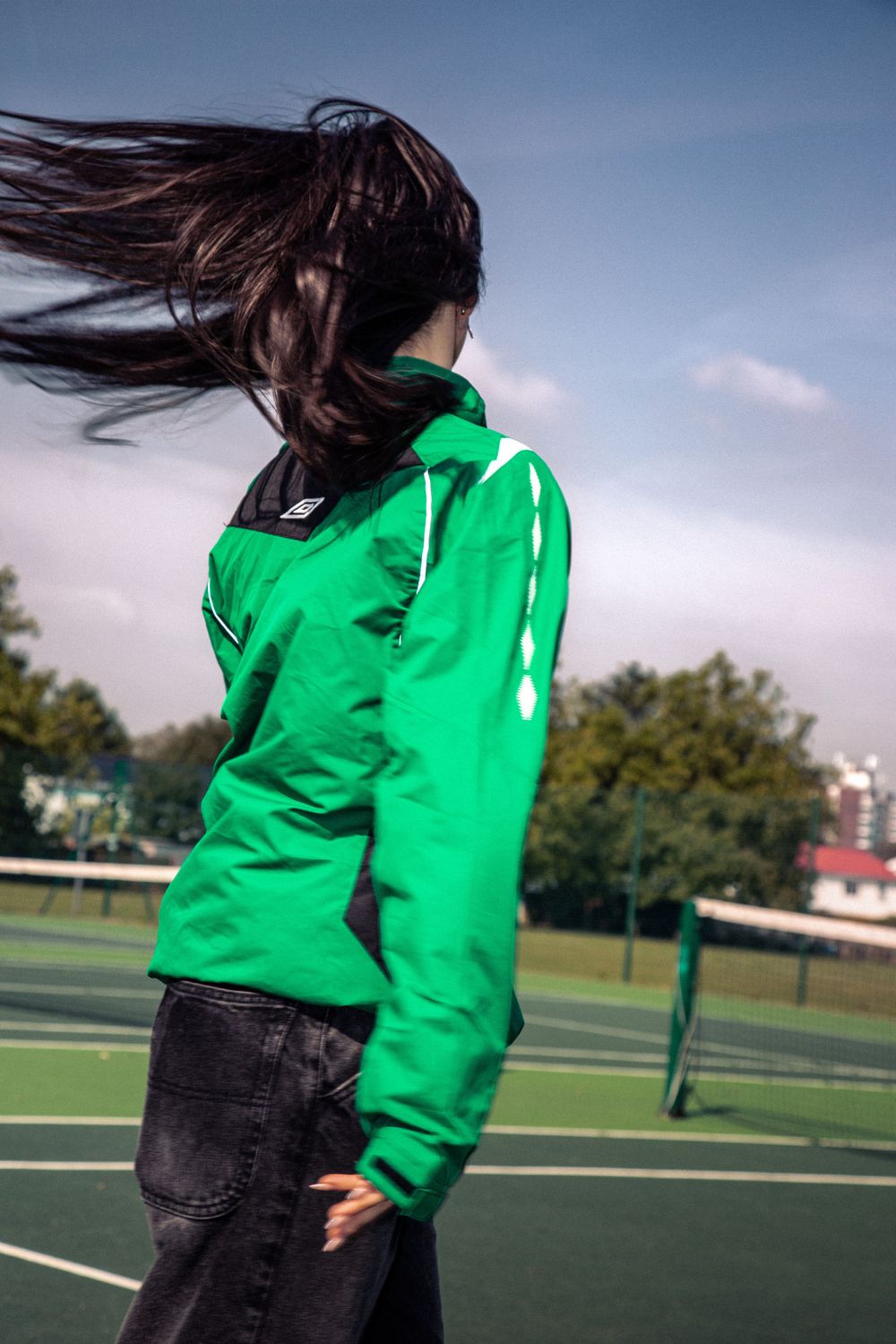 Person in vibrant green hoodie with long flowing dark hair on a sports field.