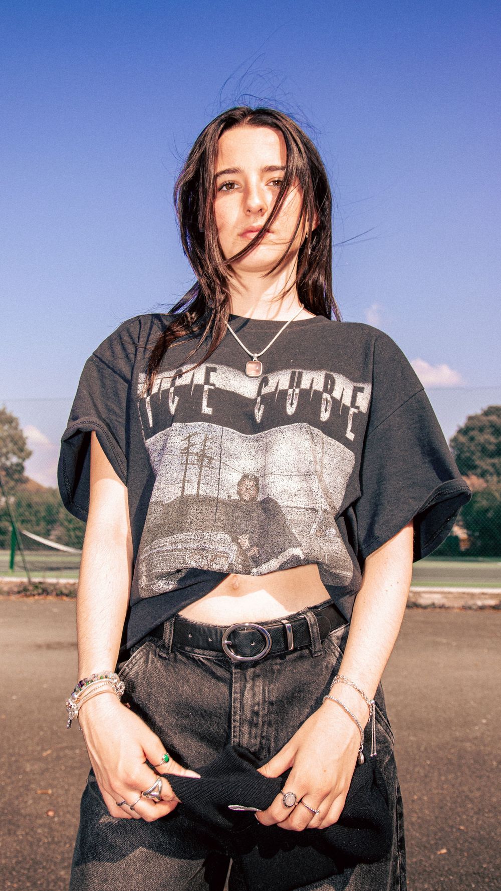 Urban fashion portrait showcasing a cropped graphic t-shirt and dark denim against a bright blue sky.