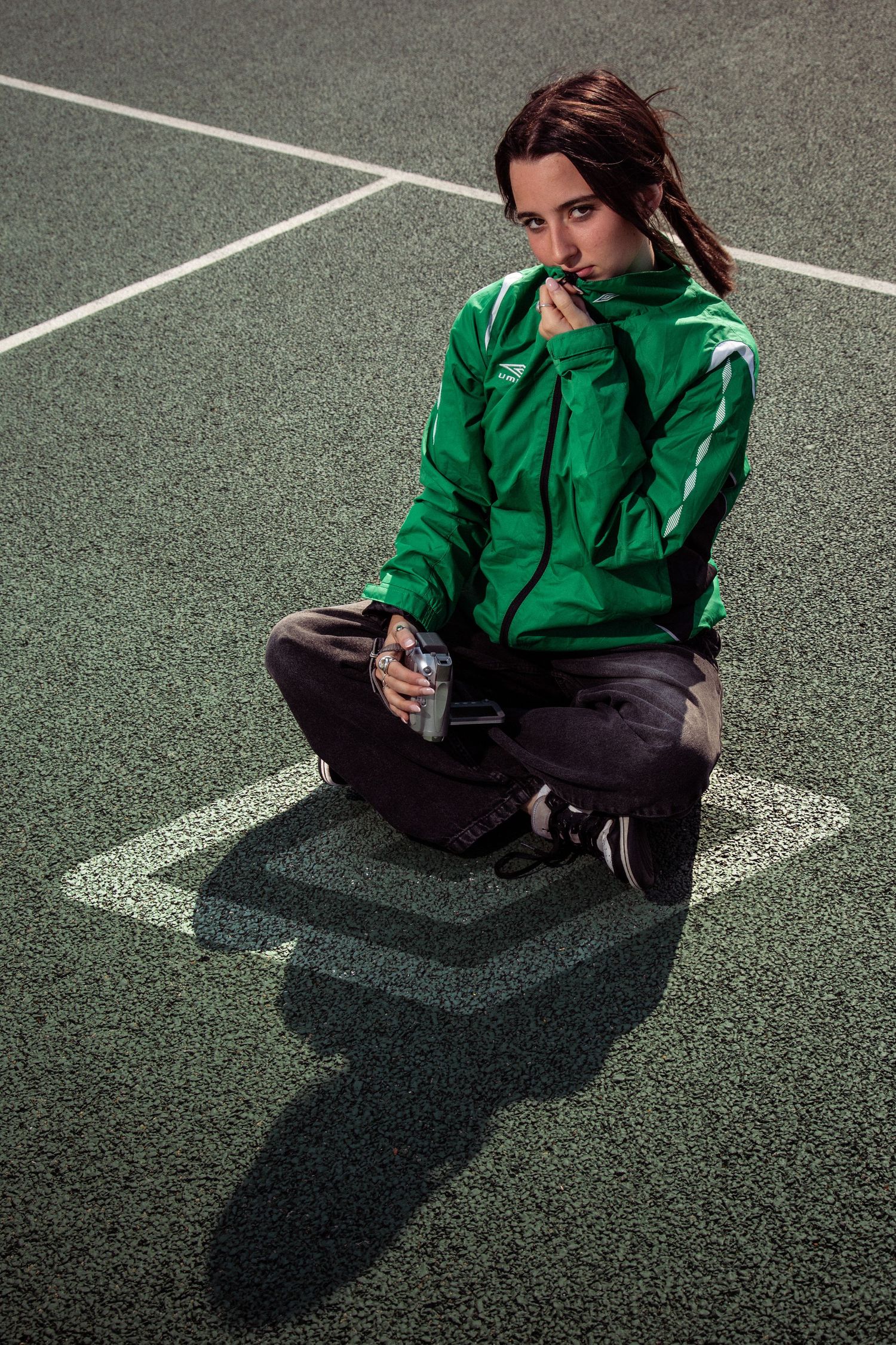Artistic portrait on a tennis court featuring vibrant green jacket and casual streetwear ensemble.