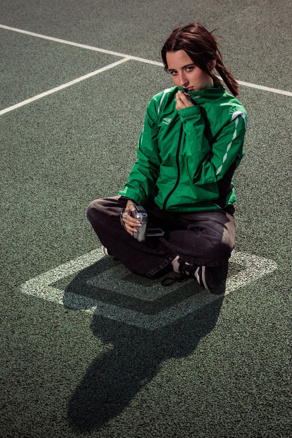 Artistic portrait on a tennis court featuring vibrant green jacket and casual streetwear ensemble.