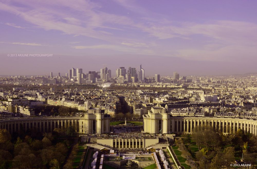 Aerial view of Paris cityscape with Trocadero gardens and La Defense business district in the background under purple sky.