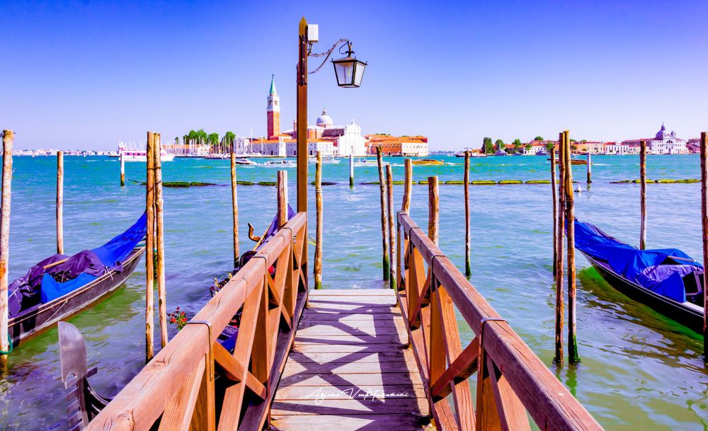 Traditional wooden dock with blue gondolas moored along the waterfront in Venice's turquoise lagoon.
