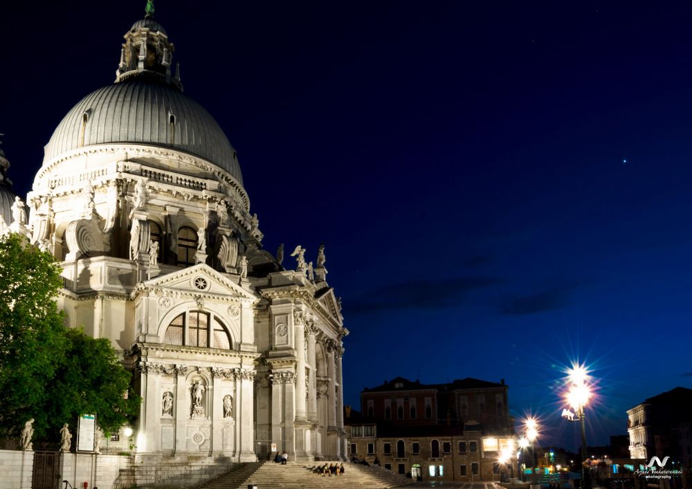 The illuminated Basilica di Santa Maria della Salute glows against a dark night sky in Venice, Italy.