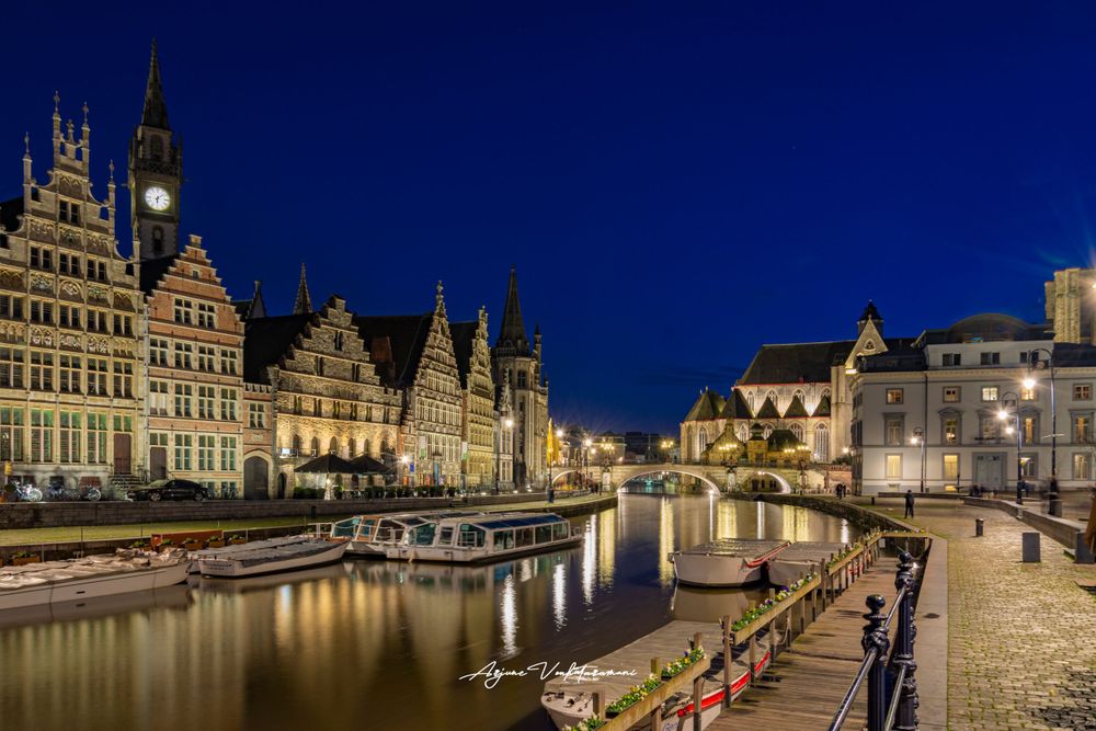Historic medieval buildings and waterfront along Graslei harbor in Ghent Belgium illuminated at night with reflections on water.