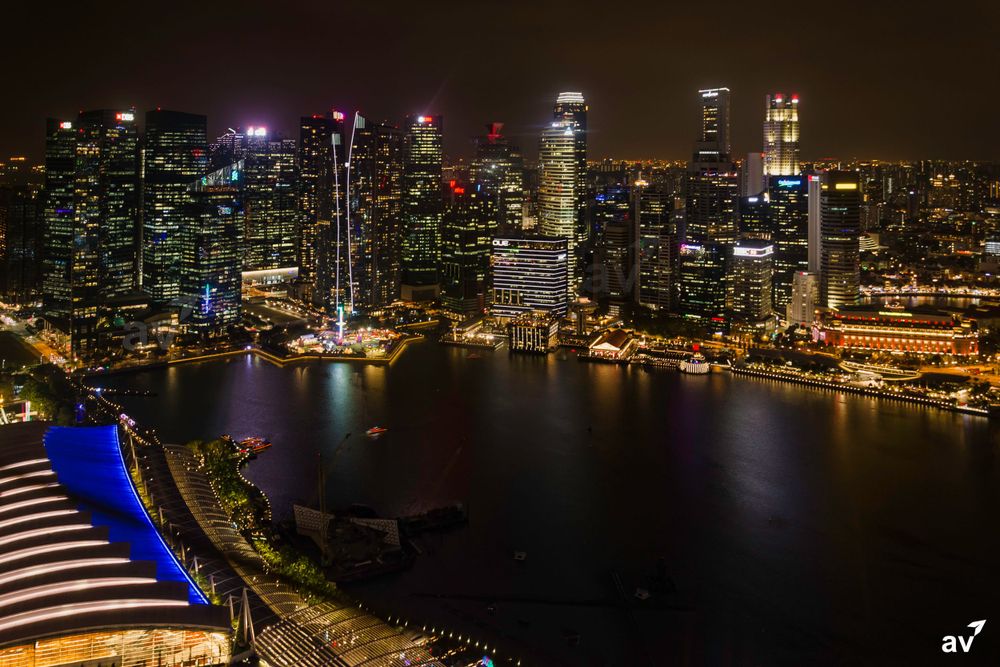 Illuminated Singapore skyline at night with Marina Bay Sands and glowing skyscrapers reflecting on dark waters.