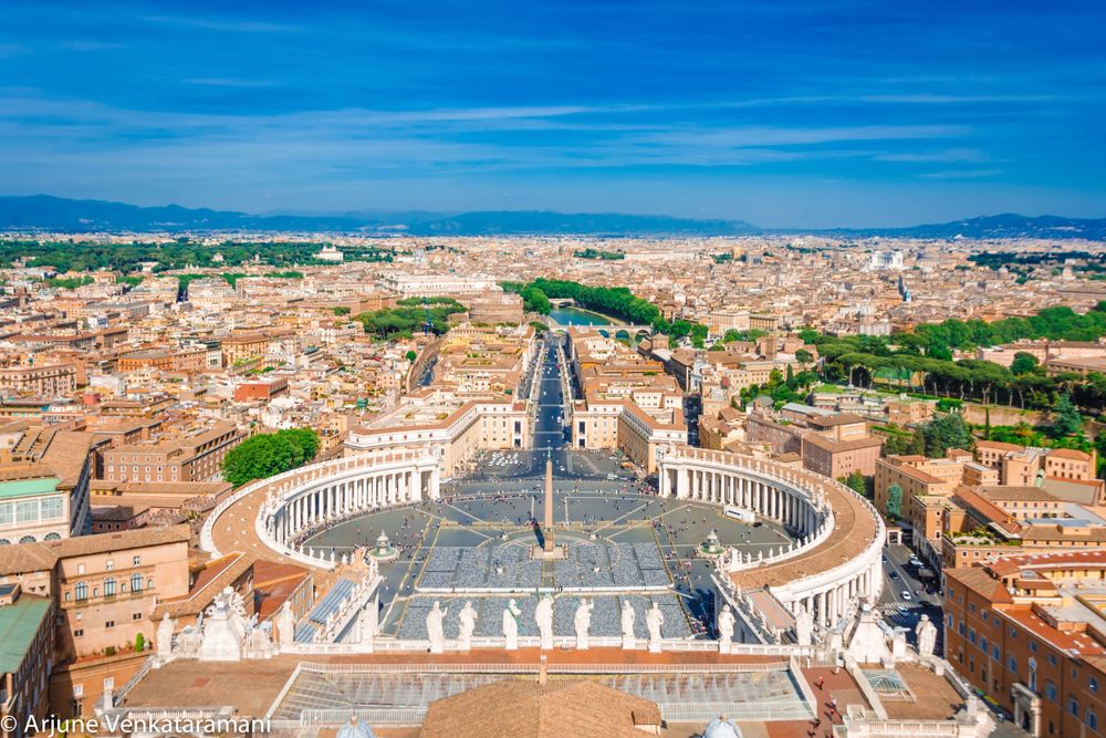 Aerial view of St. Peter's Square and Vatican City with its iconic colonnade and surrounding Rome cityscape.