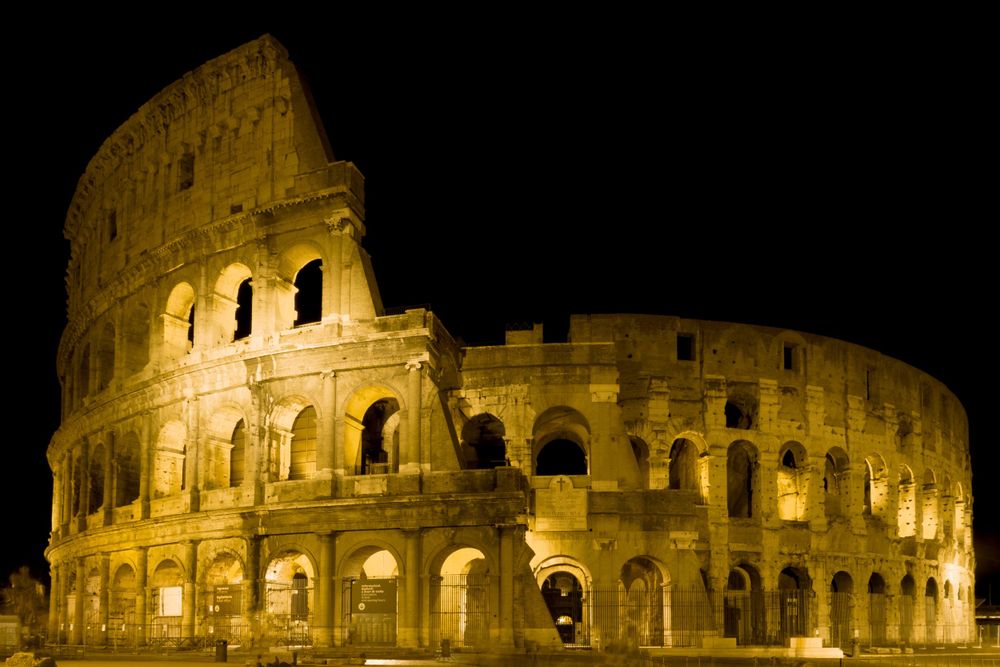 The iconic Roman Colosseum illuminated at night with golden lights against a dark sky in Rome, Italy.