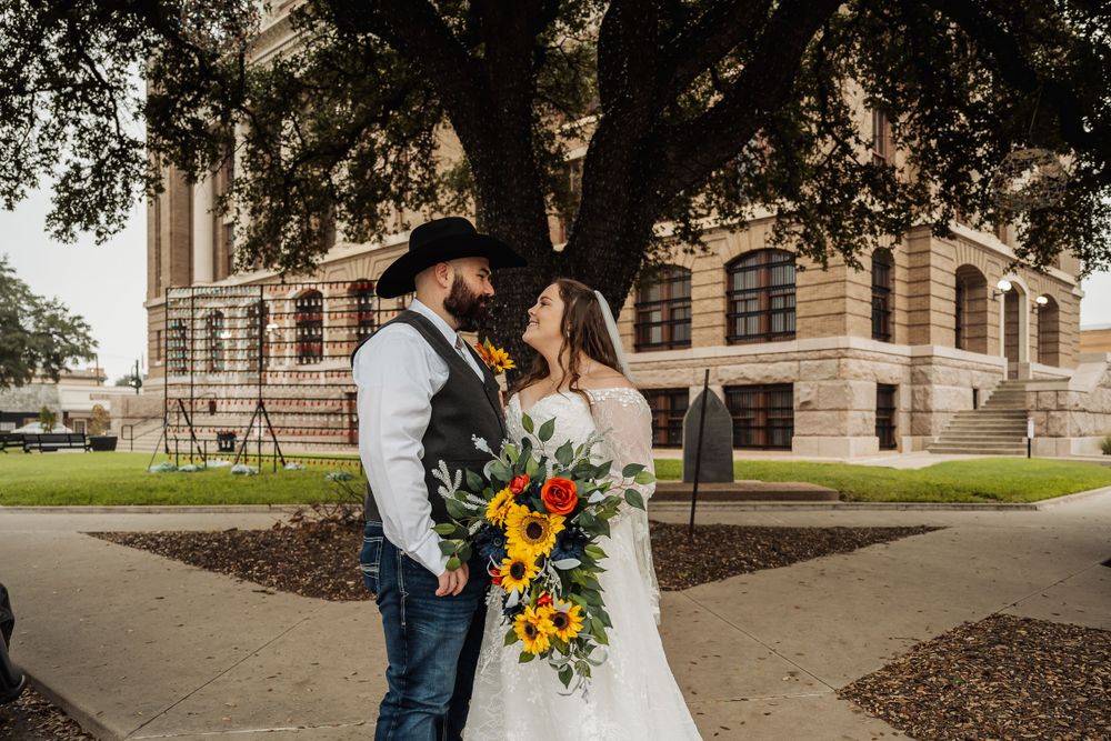 A western-themed wedding couple shares a romantic moment outside a courthouse with sunflowers.