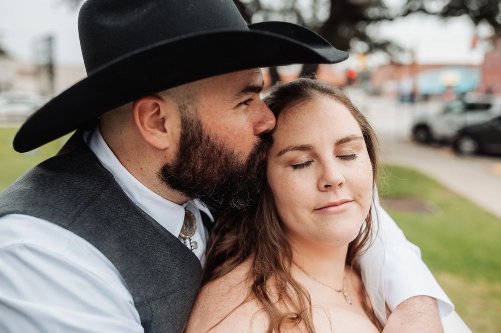 An intimate wedding portrait shows a tender moment between western-styled newlyweds outdoors.