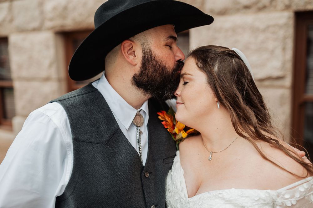 A tender moment between newlyweds with western styling during their outdoor wedding photoshoot.