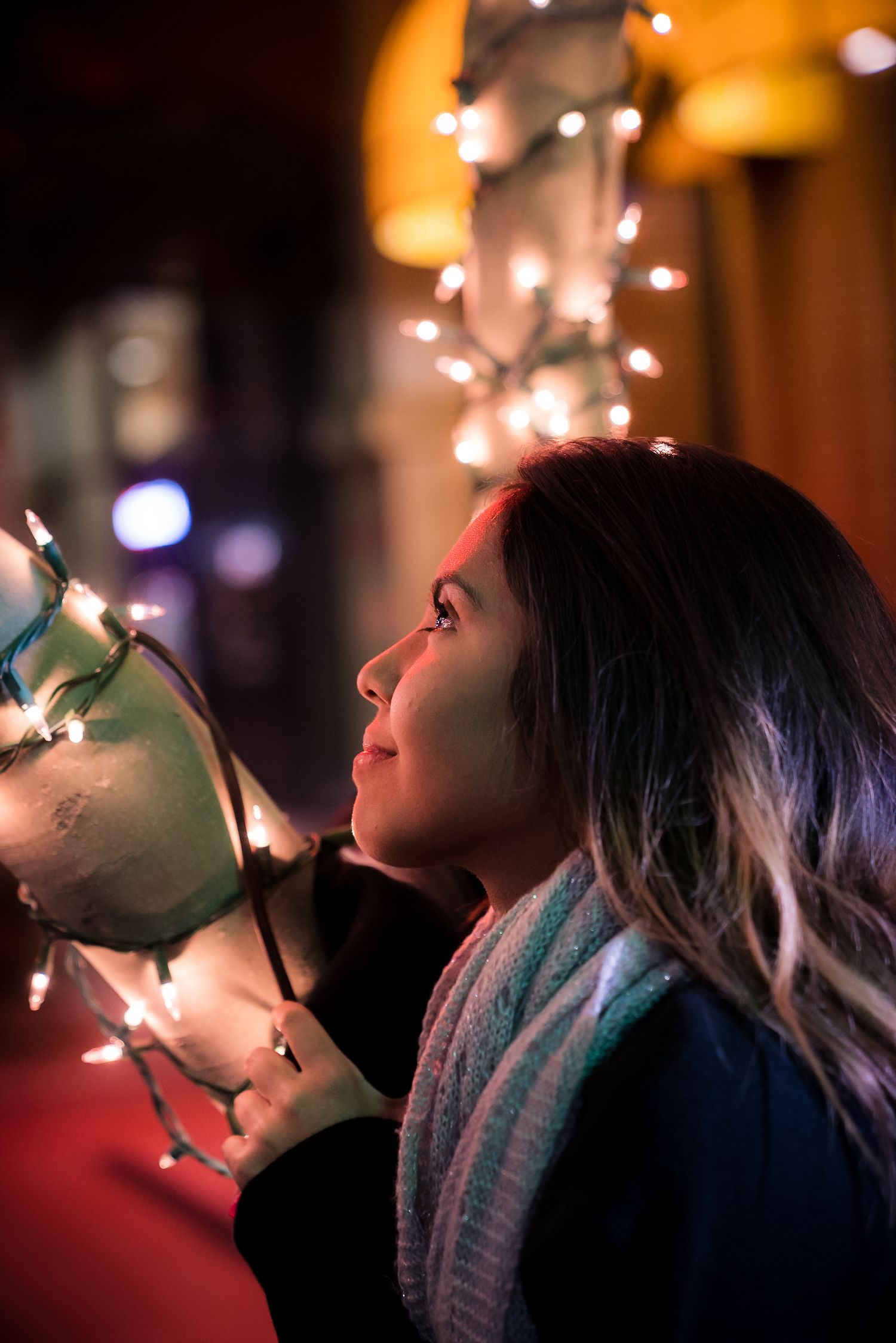 Person in cozy winter attire gazes up at glowing string lights in a dreamy nighttime scene.