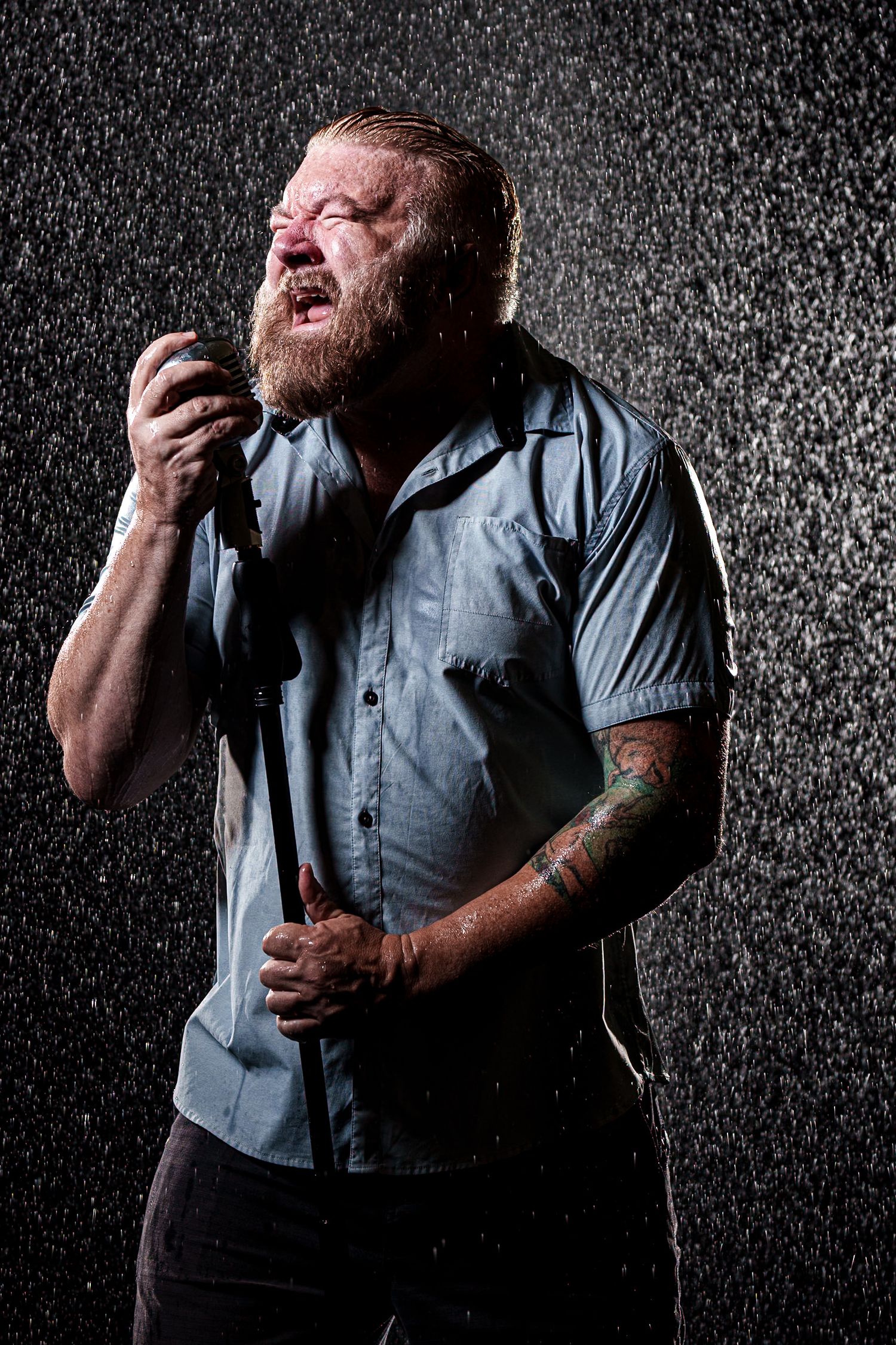 Dramatic portrait of singer performing passionately in rain against dark background.