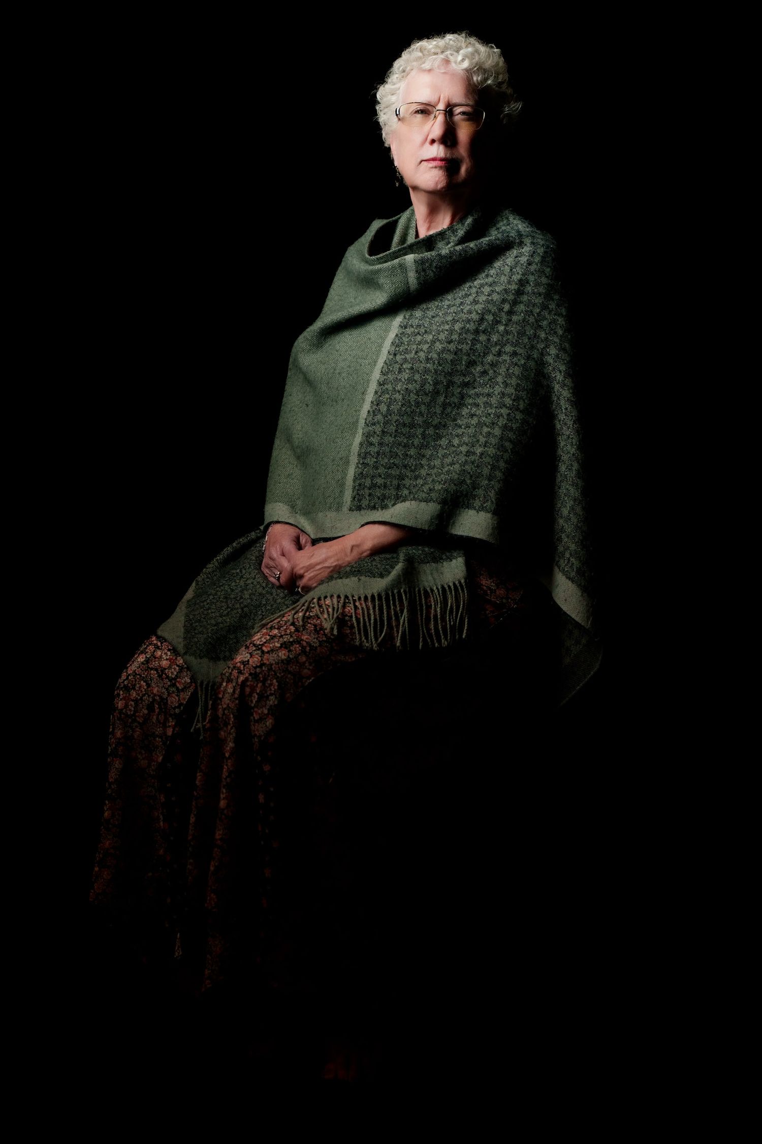 Artistic portrait of senior woman in green shawl against black background.