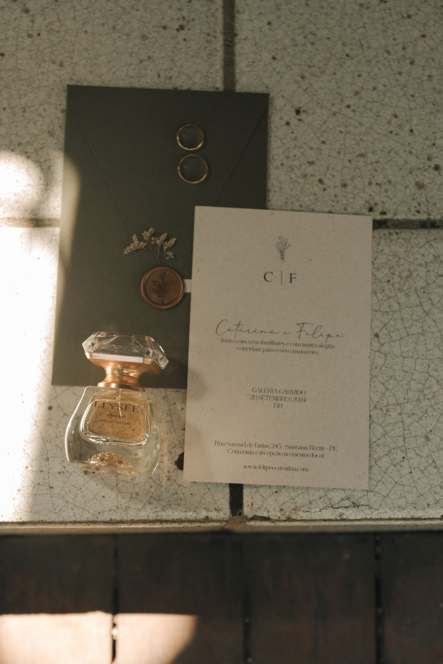 Wedding stationery with perfume bottle and rings arranged in soft lighting.