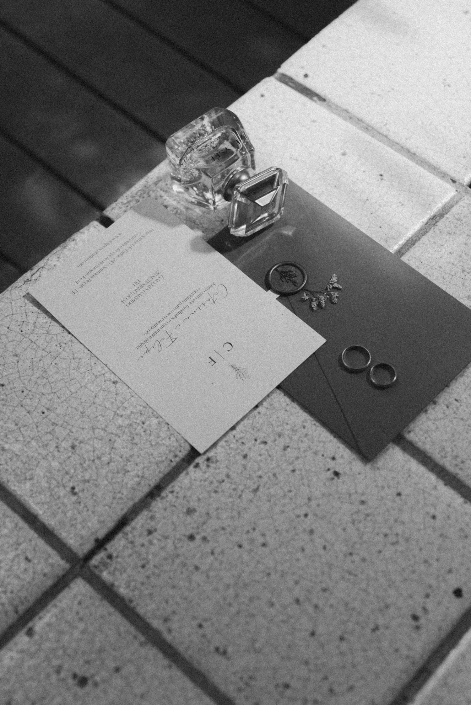 Wedding rings and invitation details arranged on a light colored surface in black and white.
