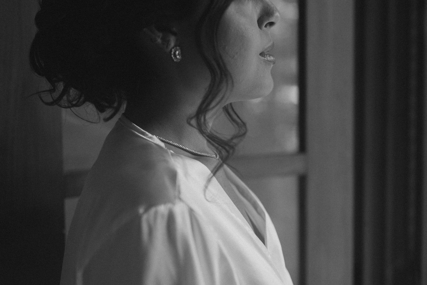 Black and white portrait of someone in a white robe looking to the side with soft window light.