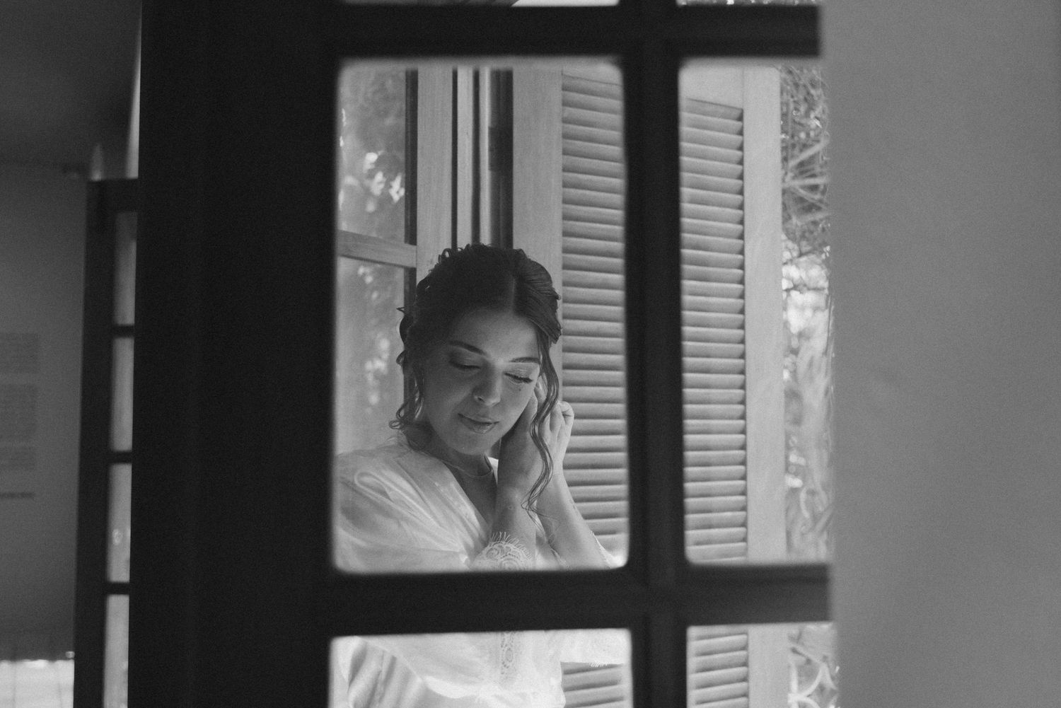 Person in white looking through window panes while smiling in a black and white photograph.