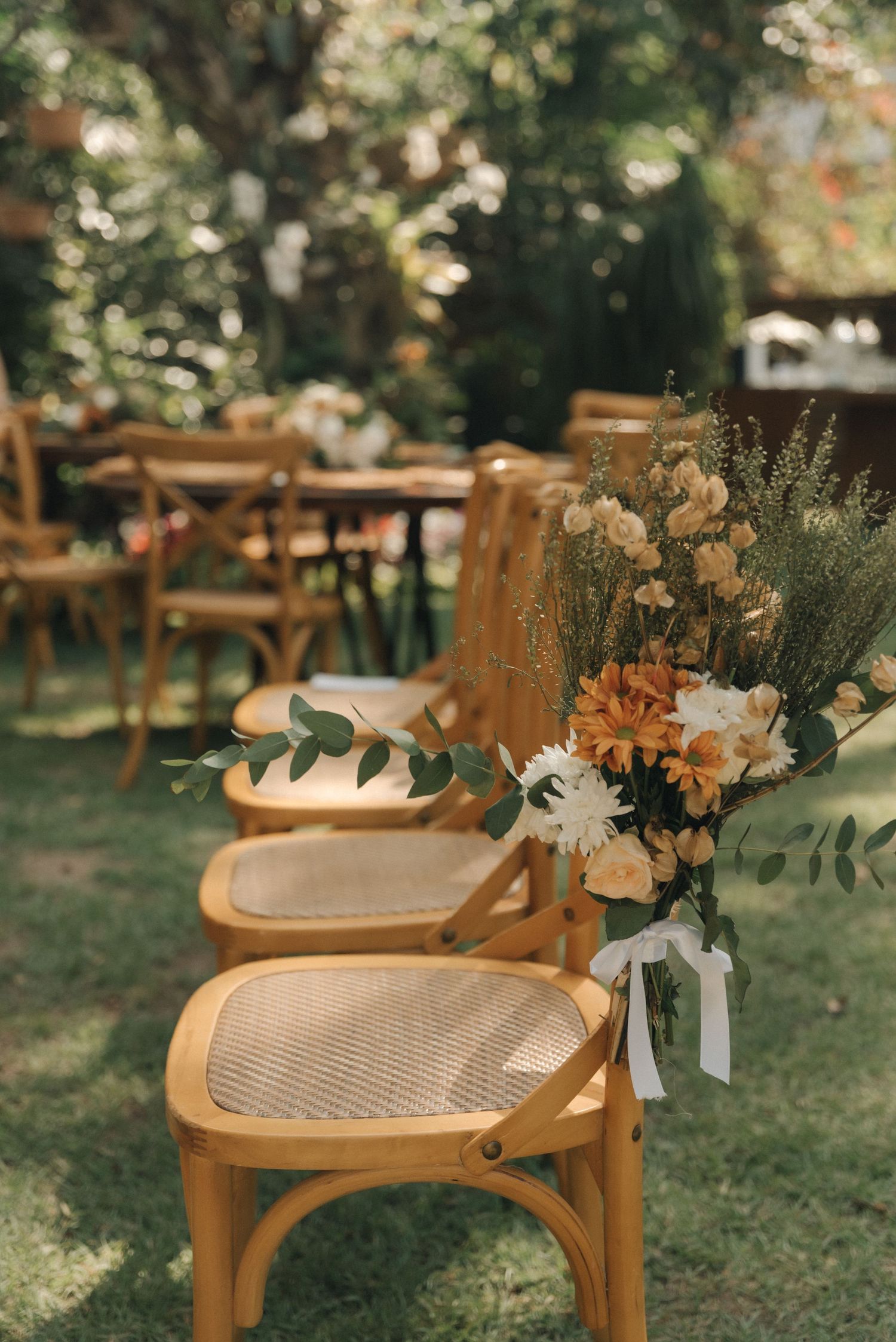 Wedding ceremony chairs decorated with floral arrangements in an outdoor garden setting.