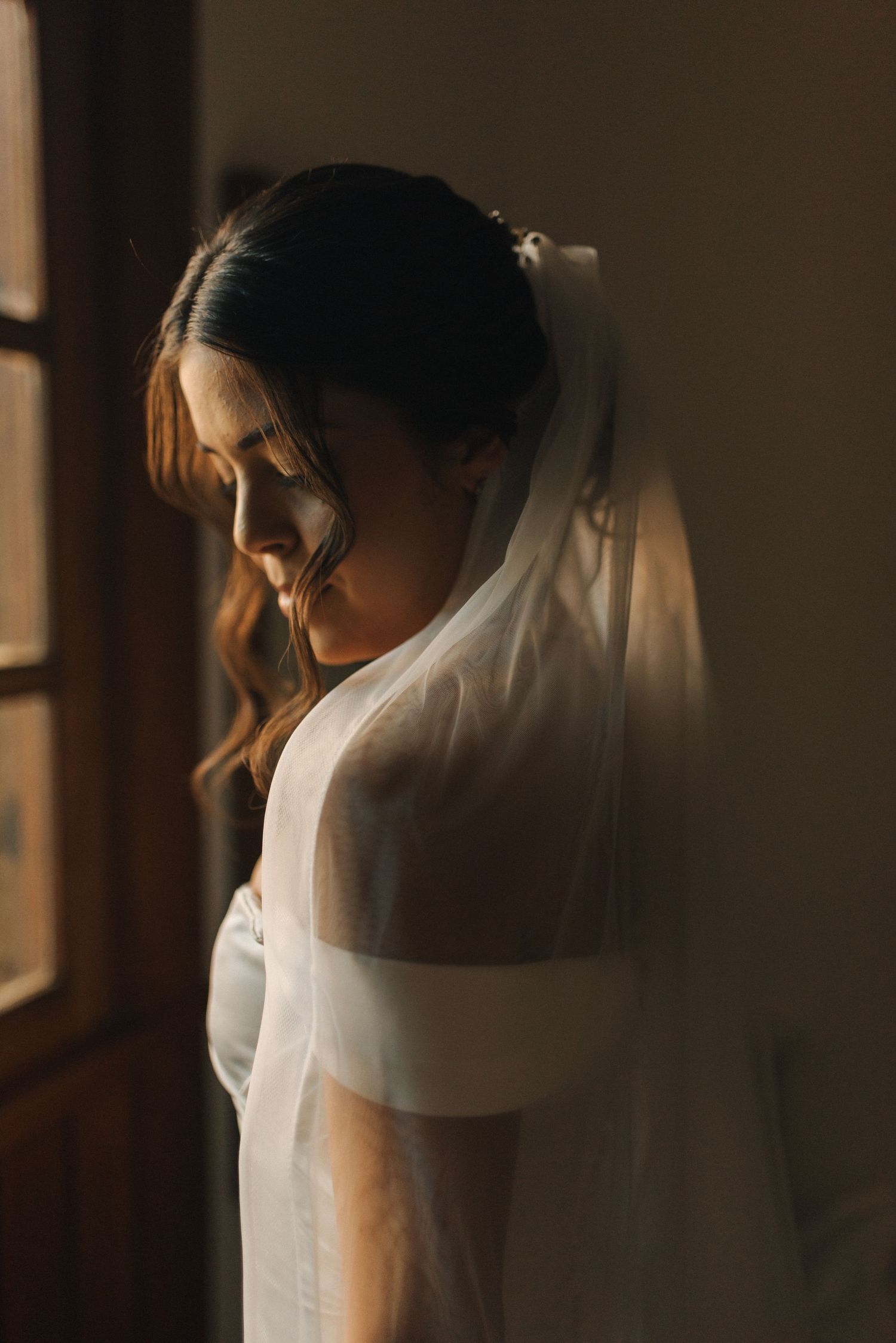 Intimate bridal photograph showing delicate veil details and off-shoulder wedding dress in window light.