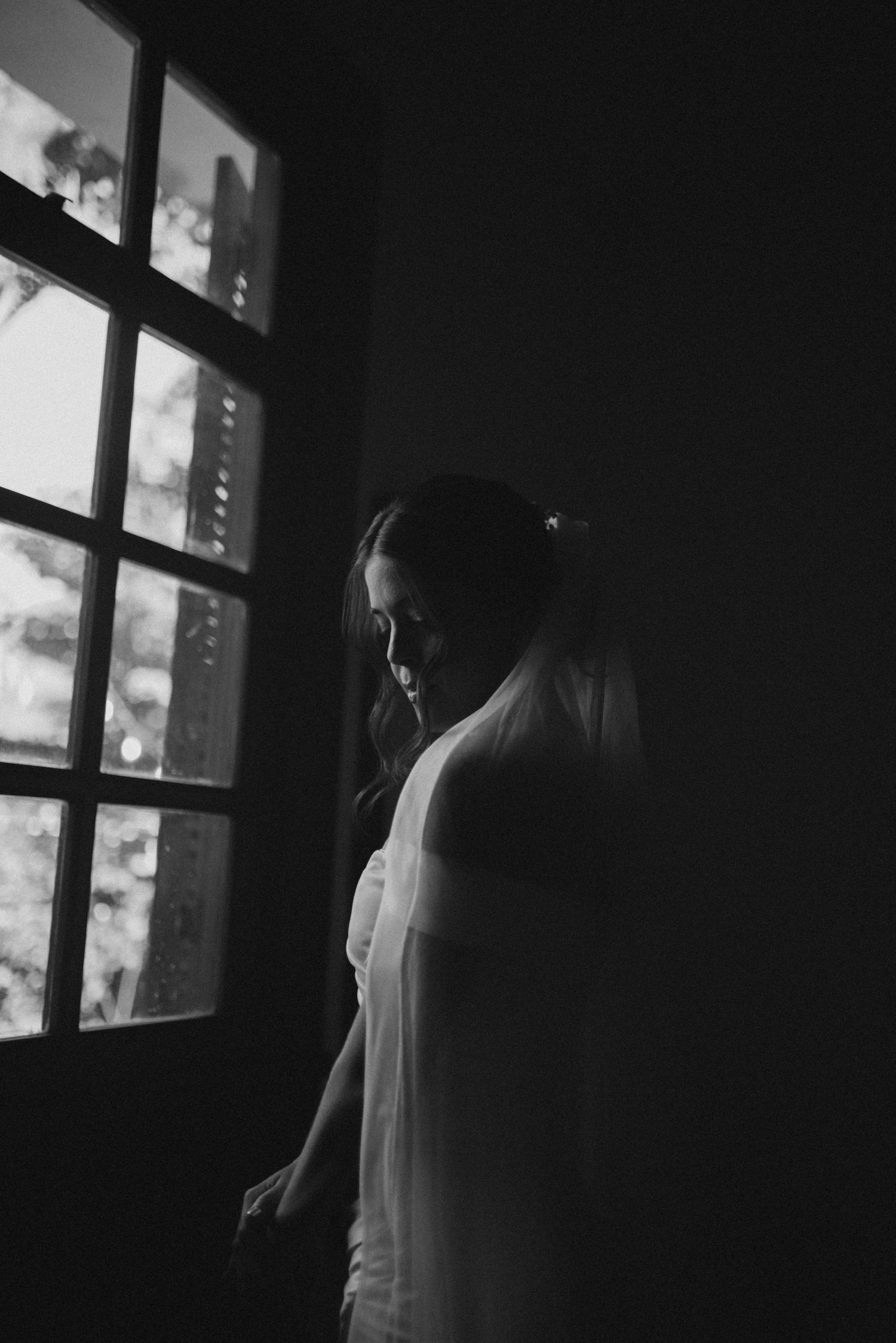 Dramatic black and white silhouette of a bride standing by a window.