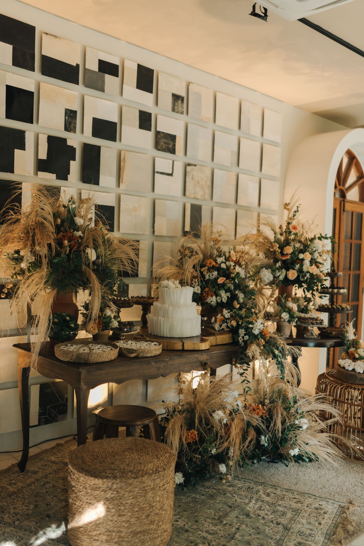 Elegant wedding dessert table with floral arrangements, pampas grass, and tiered cakes.