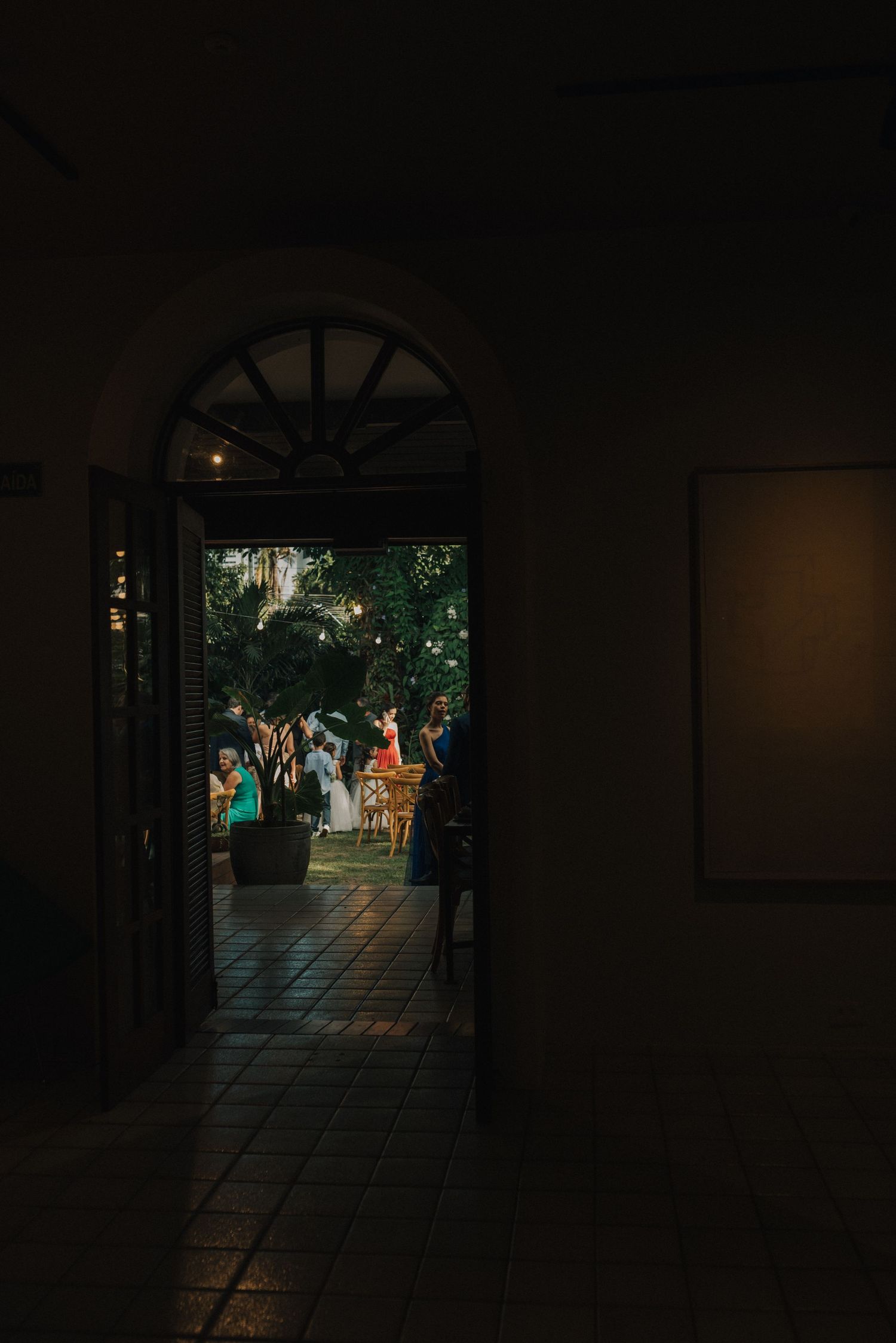Arched doorway frames a view of wedding guests gathered outdoors in a garden setting at dusk.